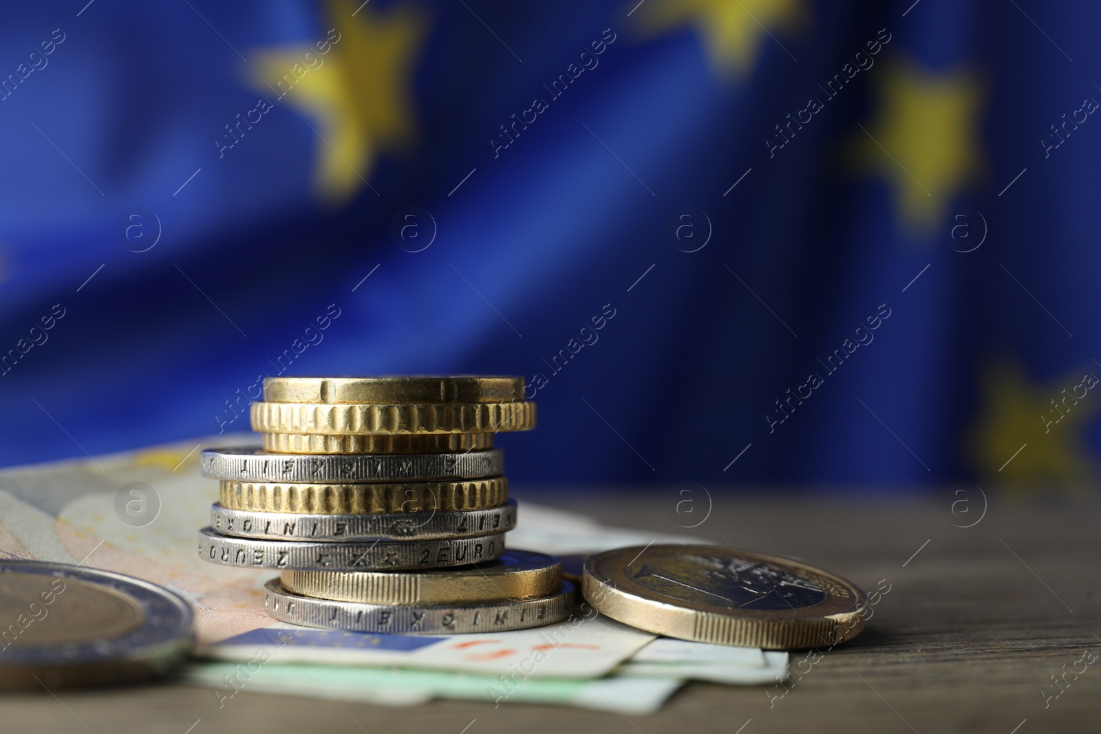 Photo of Coins and banknotes on wooden table against European Union flag, space for text