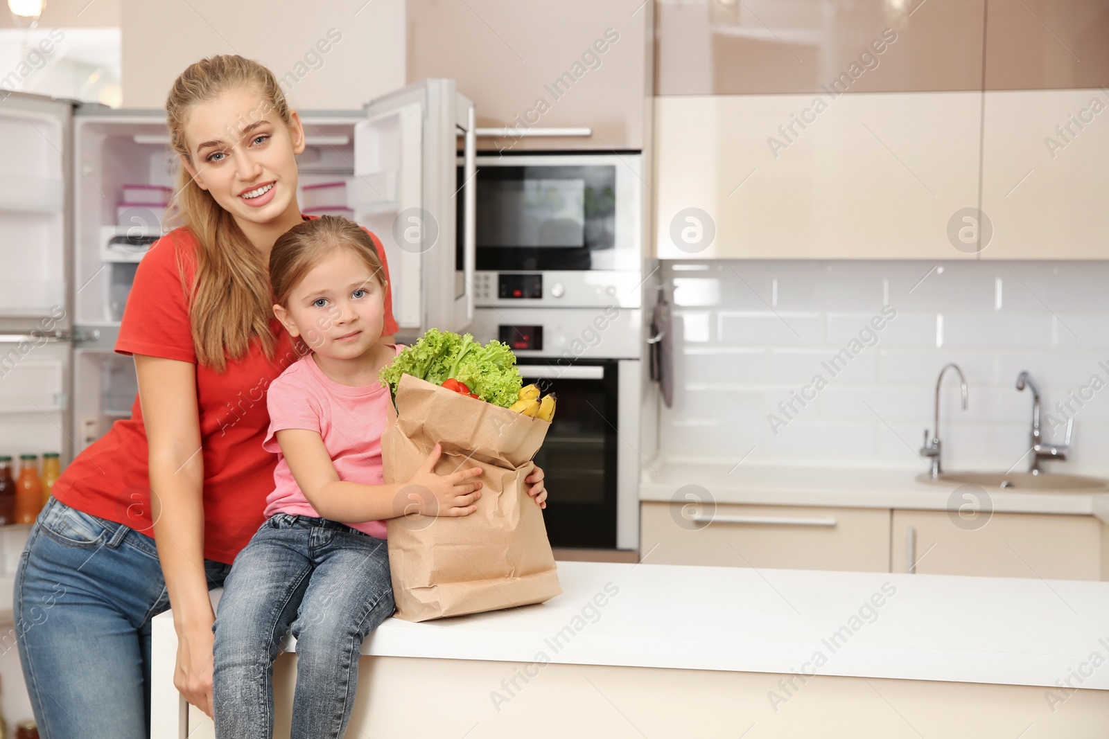 Photo of Young mother and daughter with food in paper bag at home