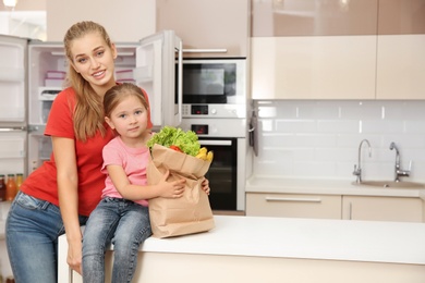 Young mother and daughter with food in paper bag at home