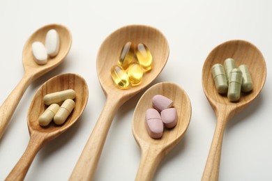 Photo of Vitamin capsules in wooden spoons on white background, closeup