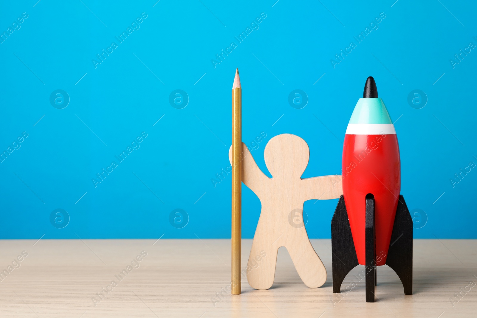 Photo of Bright toy rocket, human model and pencil on white wooden desk. Space for text