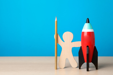 Photo of Bright toy rocket, human model and pencil on white wooden desk. Space for text