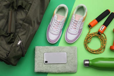 Gym bag and sports equipment on green background, flat lay