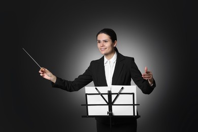 Photo of Happy professional conductor with baton and note stand on black background