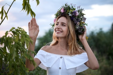 Young woman wearing wreath made of beautiful flowers outdoors