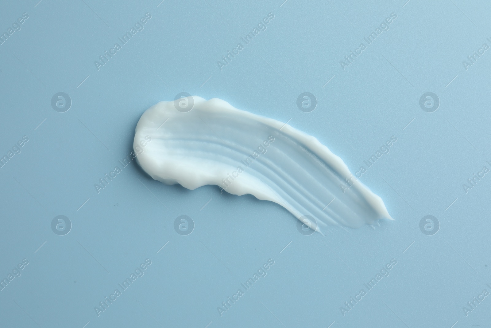 Photo of Sample of hand cream on light blue background, top view