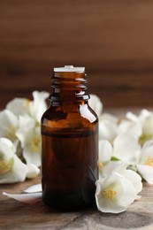 Photo of Jasmine essential oil and fresh flowers on wooden table