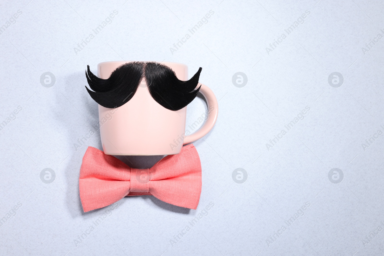 Photo of Man's face made of artificial mustache, bow tie and glasses on light grey background, top view. Space for text