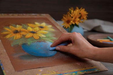 Photo of Woman drawing beautiful flowers in vase on paper with pastel at table, closeup