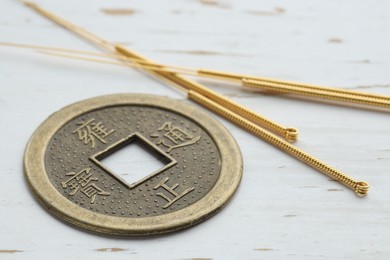 Acupuncture needles and Chinese coin on white wooden table, closeup