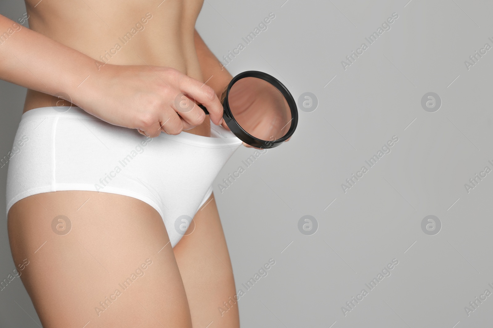 Photo of Woman examining genital herpes with magnifying glass on light grey background, closeup. Space for text