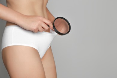 Photo of Woman examining genital herpes with magnifying glass on light grey background, closeup. Space for text