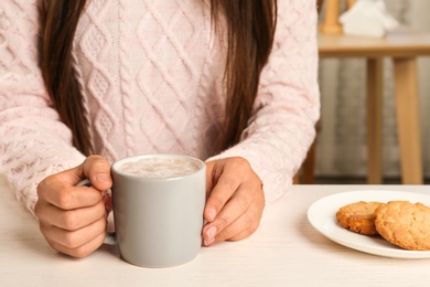 Photo of Woman holding cup of delicious cocoa drink at white table, closeup