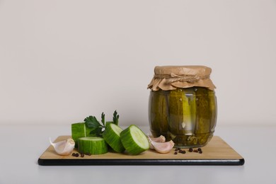 Photo of Tasty pickled cucumbers, cut vegetables and garlic on white table