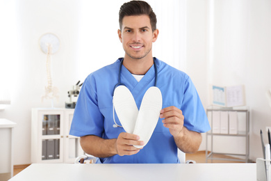 Handsome male orthopedist showing insoles in clinic