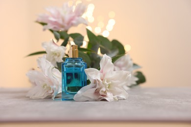 Photo of Bottle of perfume and beautiful lily flowers on table against beige background with blurred lights, closeup