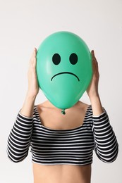 Image of Woman hiding behind green balloon with sad face on white background