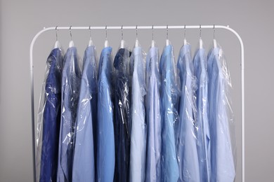 Photo of Dry-cleaning service. Many different clothes in plastic bags hanging on rack against grey background