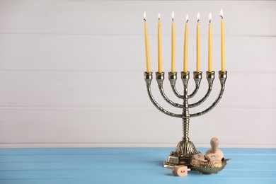 Photo of Hanukkah celebration. Menorah with burning candles and dreidels on light blue wooden table, space for text
