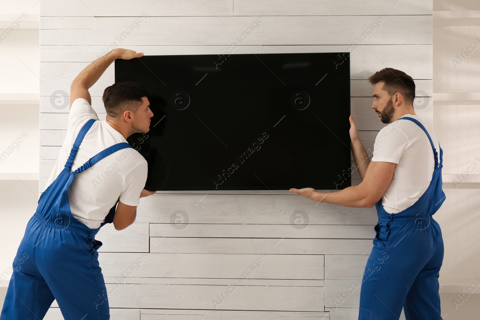 Photo of Professional technicians installing modern flat screen TV on wall indoors