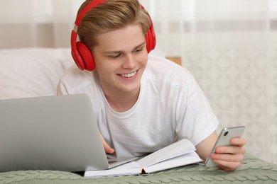 Photo of Teenage boy with smartphone and headphones using laptop at home