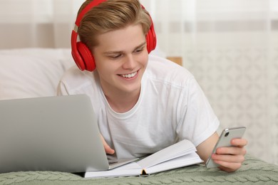 Teenage boy with smartphone and headphones using laptop at home