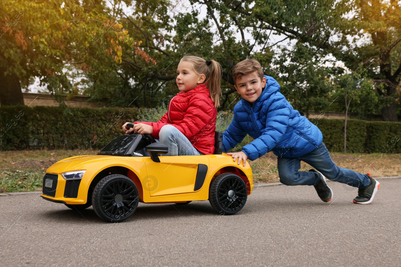 Photo of Cute boy pushing children's car with little girl outdoors