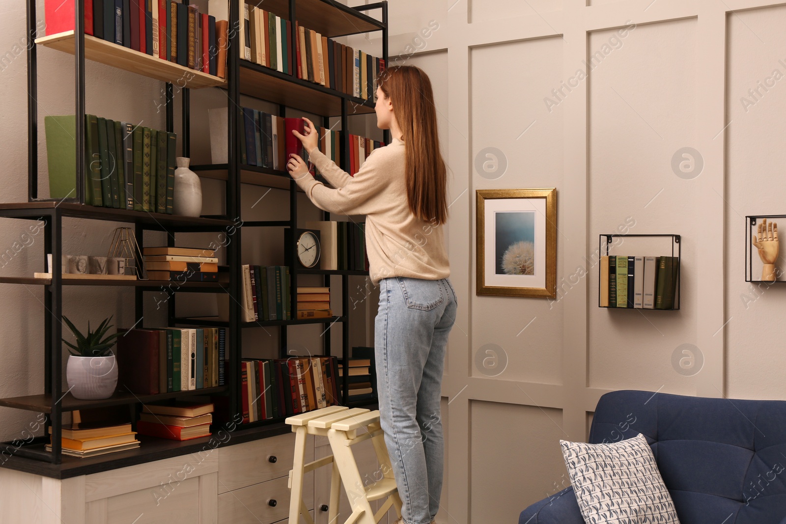 Photo of Young woman choosing book on shelf in home library