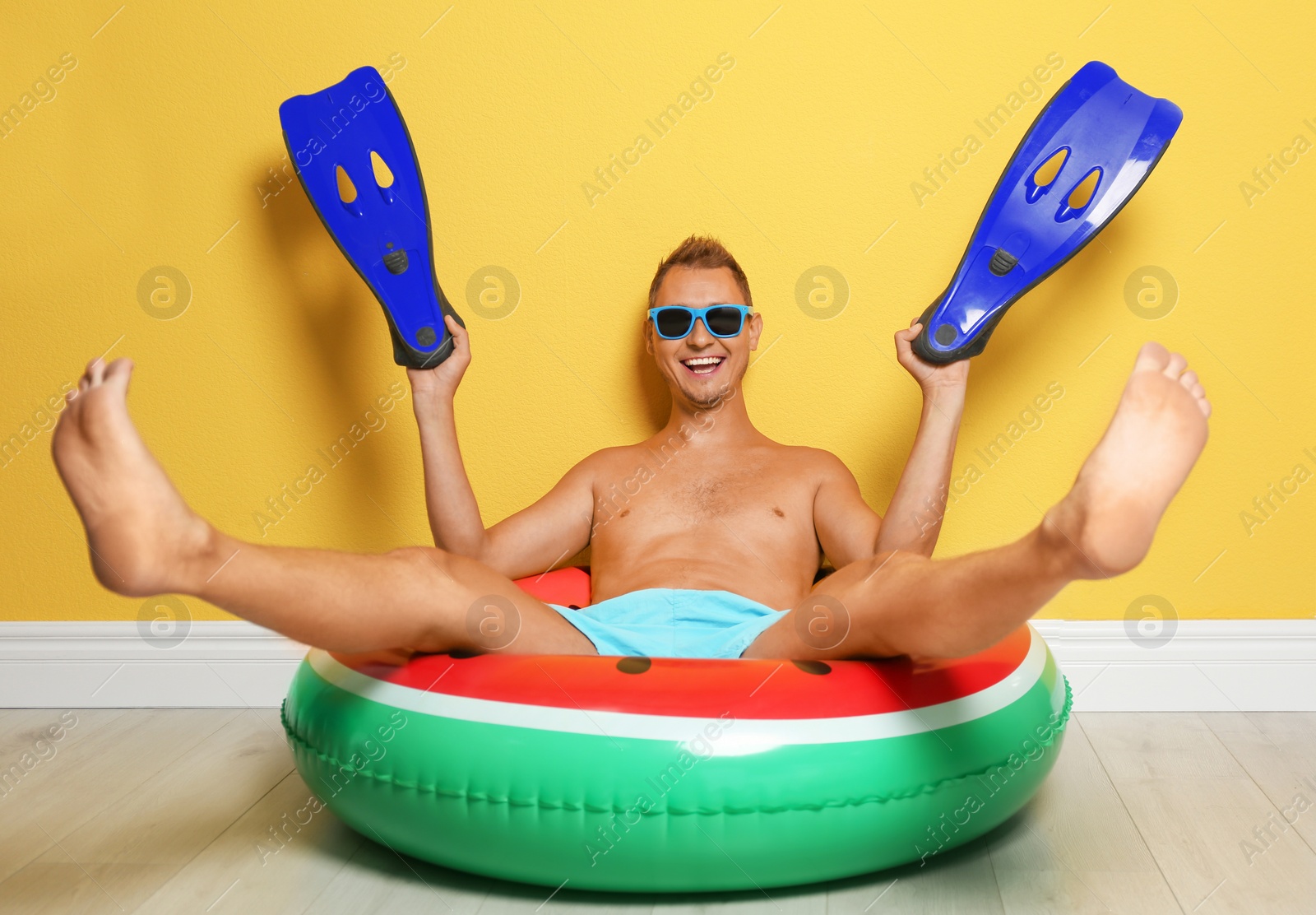 Photo of Shirtless man with inflatable ring and flippers having fun on floor near color wall