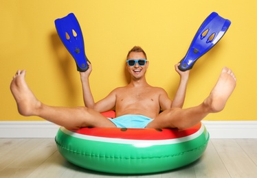 Shirtless man with inflatable ring and flippers having fun on floor near color wall