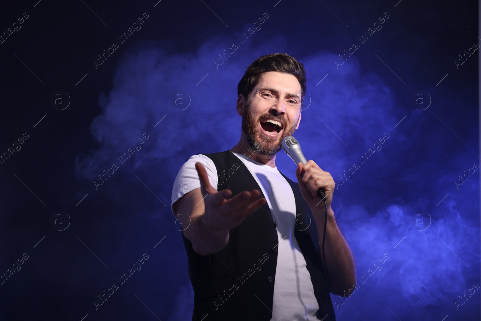 Photo of Handsome man with microphone singing on dark blue background