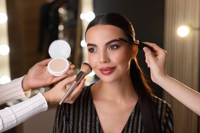 Makeup artists working with beautiful woman in dressing room