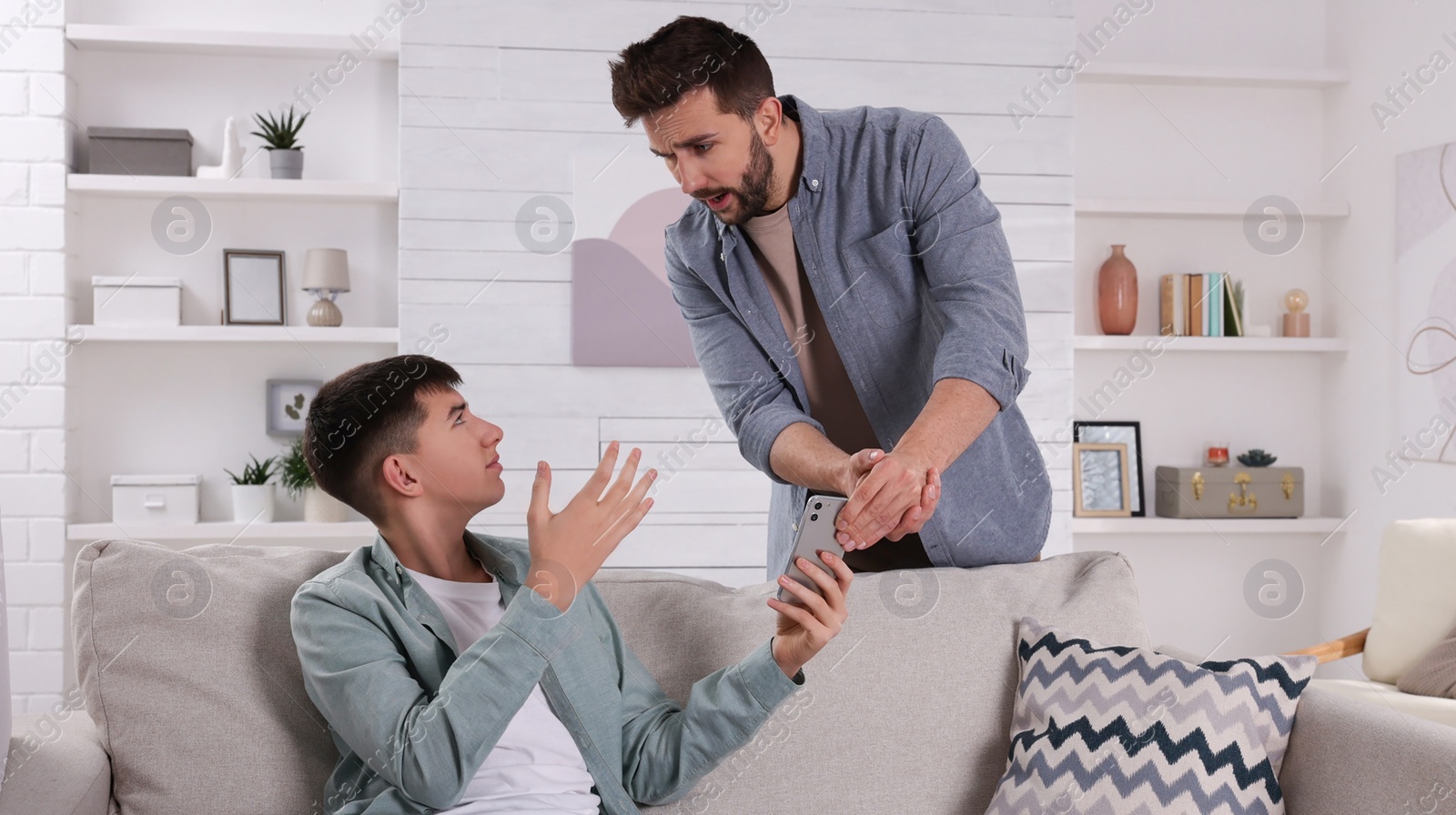 Photo of Upset father taking away phone from his son at home. Teenager problems