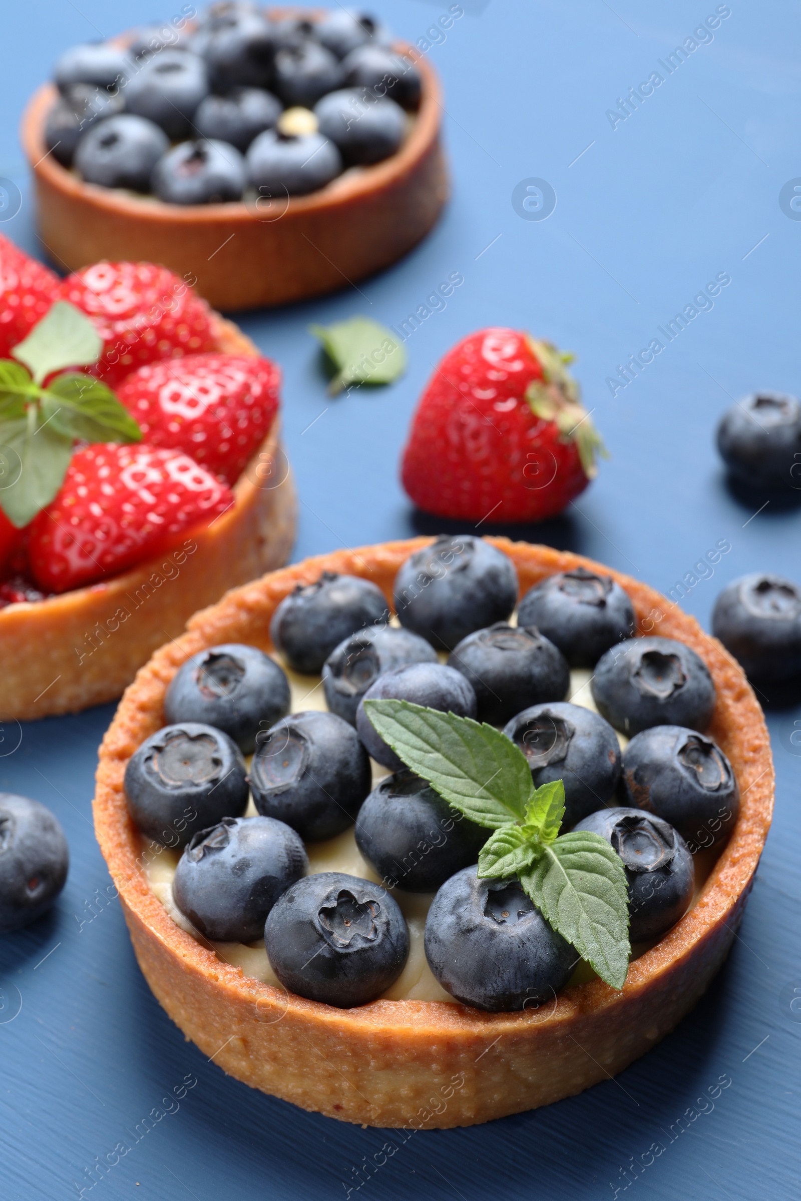 Photo of Tartlets with different fresh berries and mint on blue table. Delicious dessert