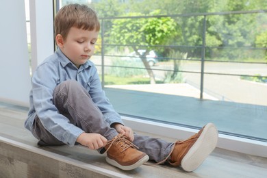 Photo of Cute little boy tying shoe laces at home, space for text