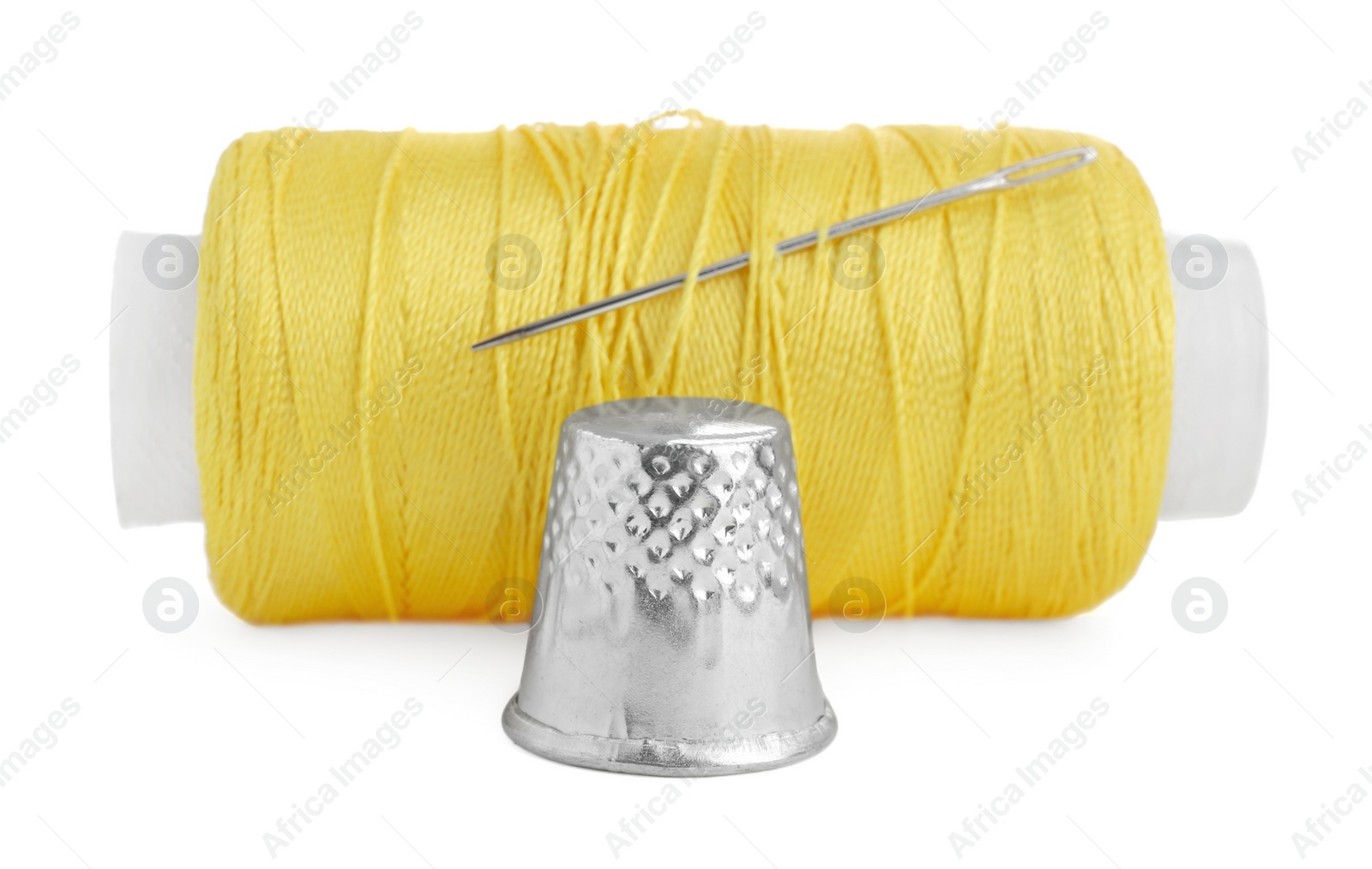 Photo of Thimble and spool of yellow sewing thread with needle isolated on white