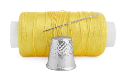 Thimble and spool of yellow sewing thread with needle isolated on white