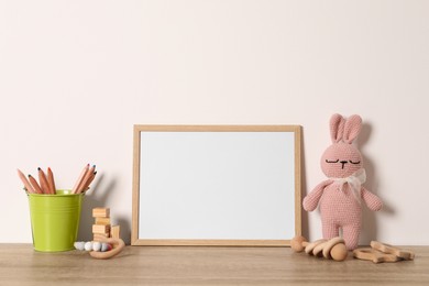 Photo of Empty square frame, stationery and different toys on wooden table