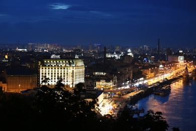 KYIV, UKRAINE - MAY 21, 2019: Beautiful view of night cityscape with illuminated buildings near river and bridge