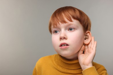 Photo of Little boy with hearing aid on grey background, space for text