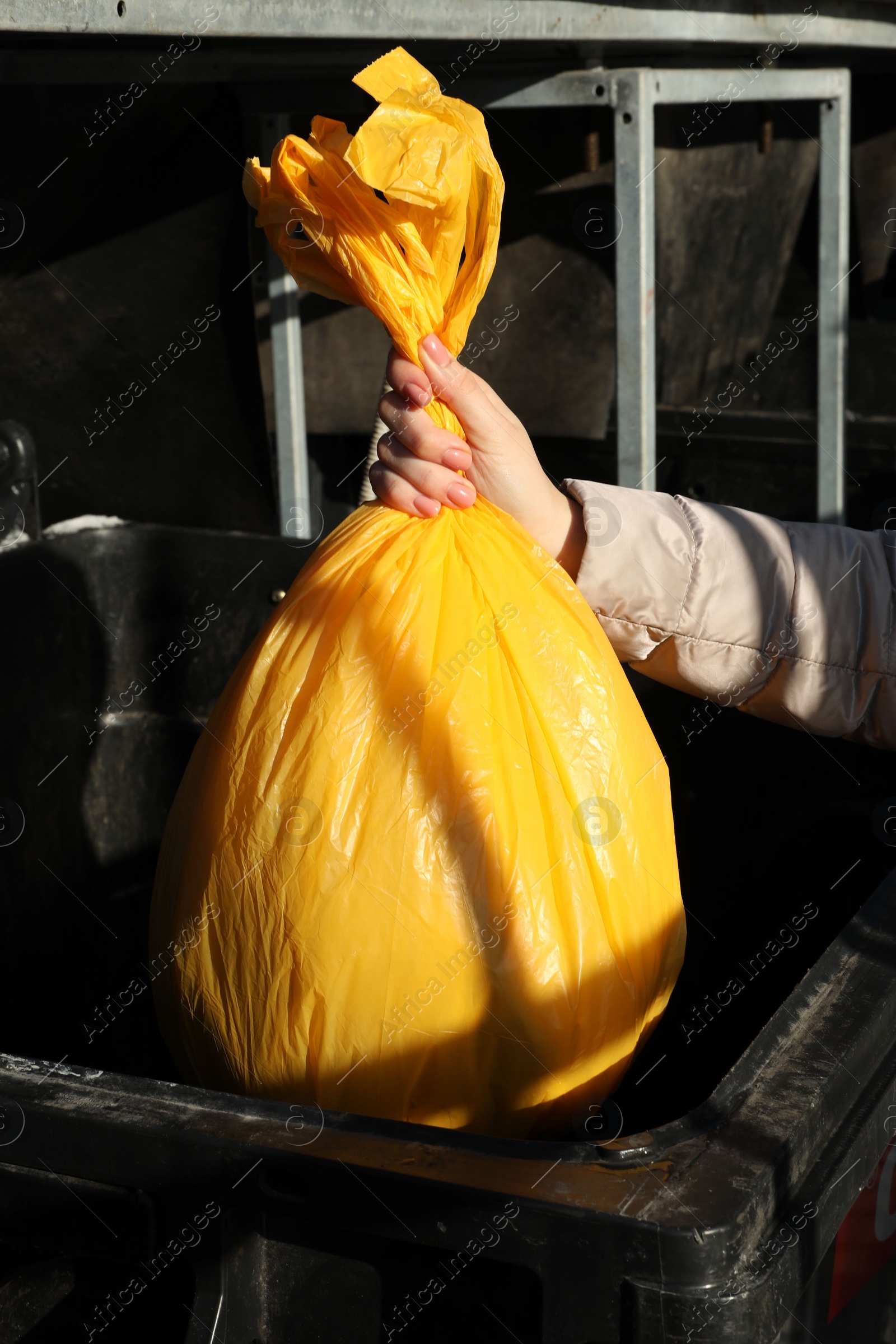 Photo of Woman throwing trash bag full of garbage in bin outdoors, closeup