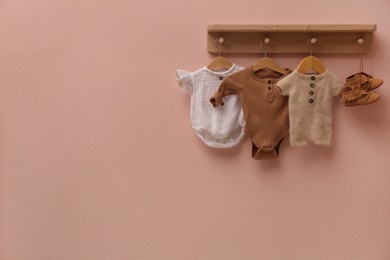 Photo of Wooden rack with cute baby clothes and shoes on pink wall indoors. Space for text