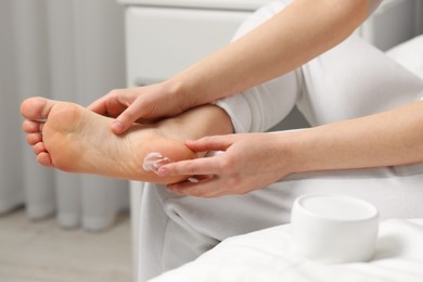 Young woman with dry skin applying cream onto her foot indoors, closeup