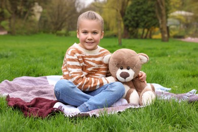 Photo of Little girl with teddy bear on plaid outdoors