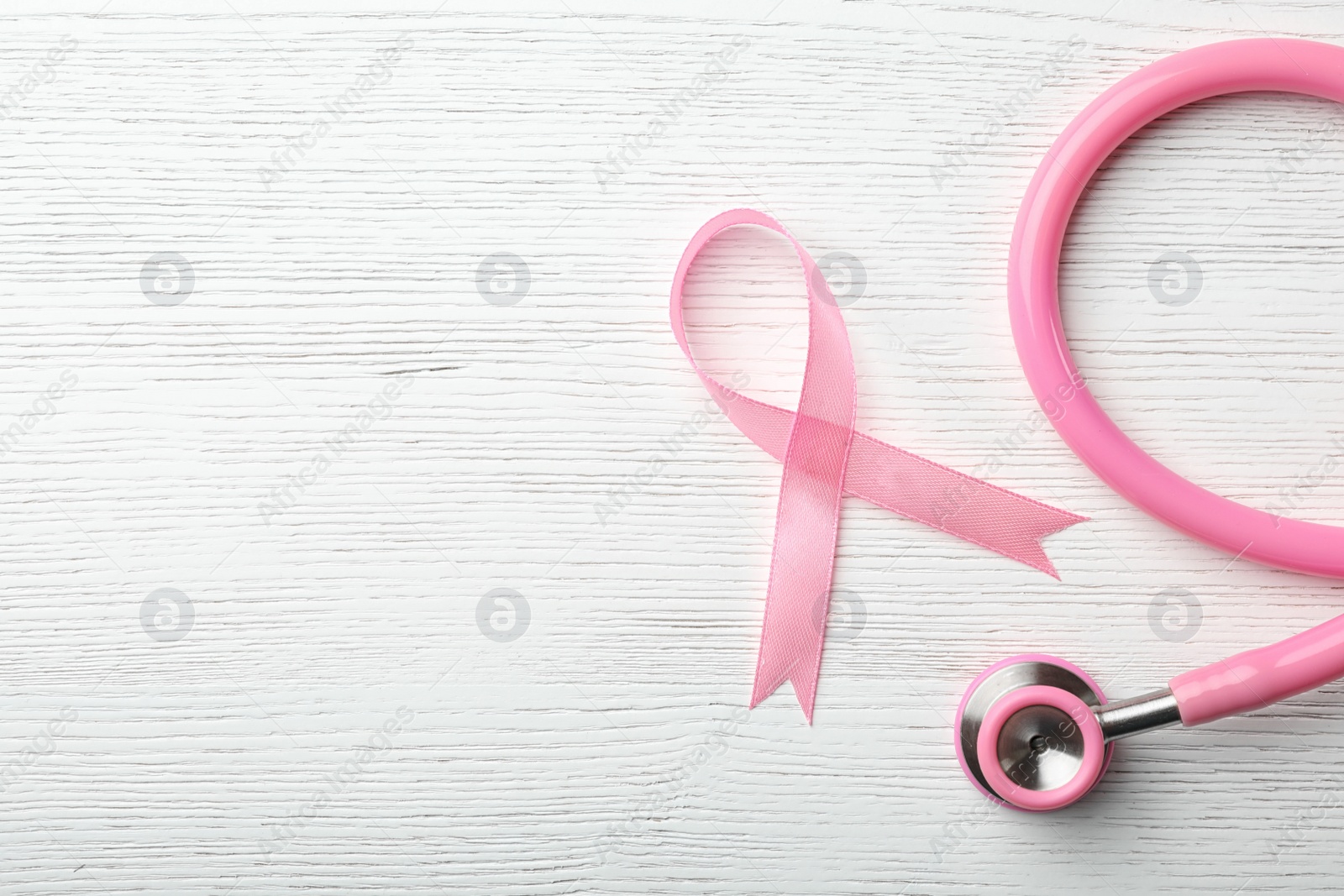 Photo of Pink ribbon and stethoscope on wooden background, top view with space for text. Breast cancer concept