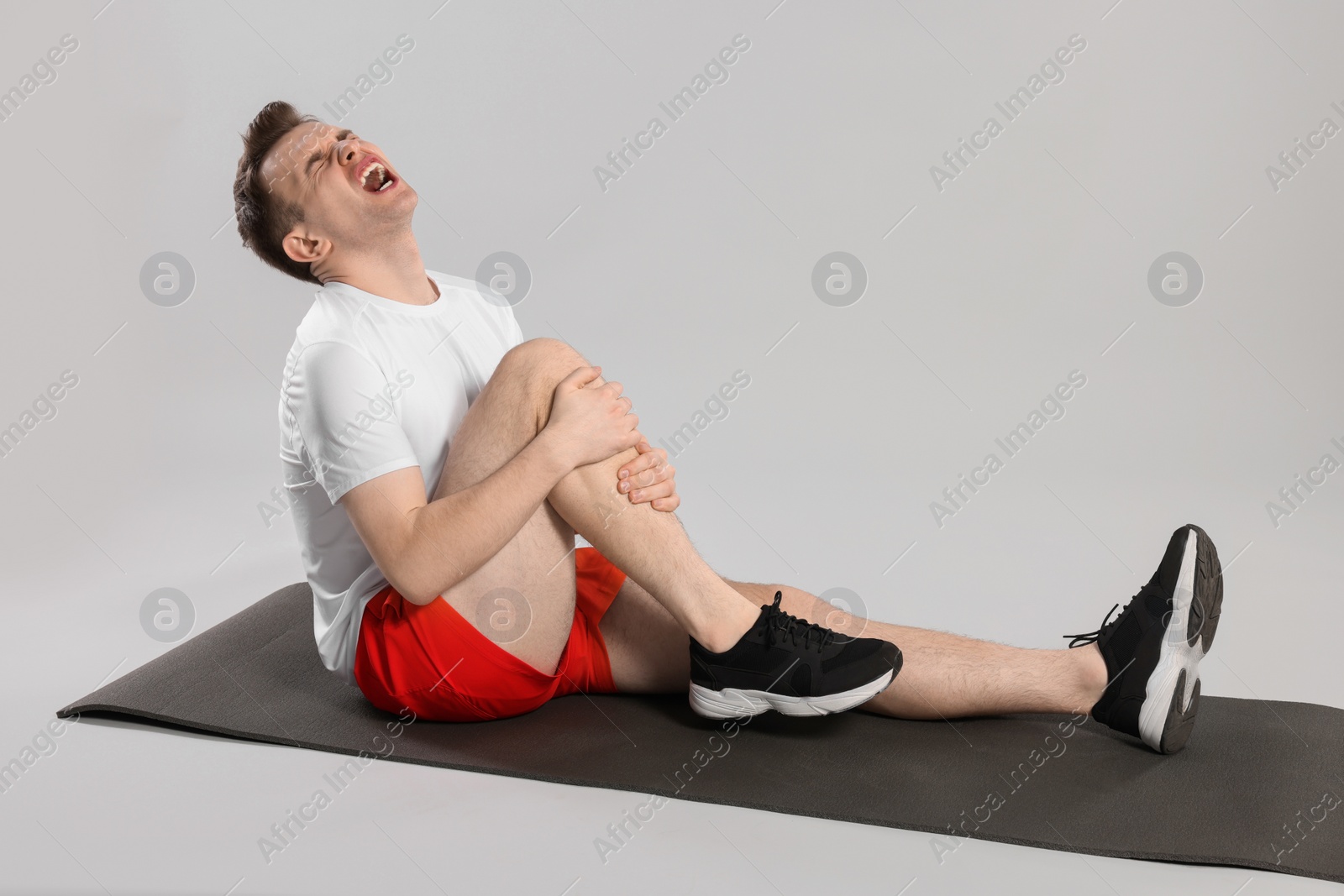 Photo of Man suffering from leg pain on mat against grey background