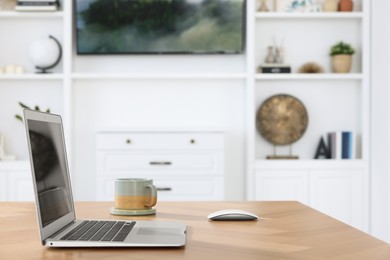 Interior design. Cosy workplace with laptop and cup on wooden table near tv area. Space for text