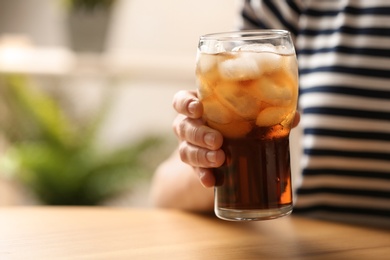 Woman holding glass of cola with ice at table, closeup. Space for text