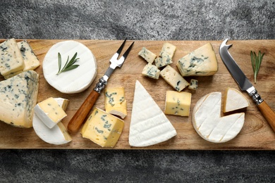 Photo of Cheese platter with specialized knife and fork on grey table, top view