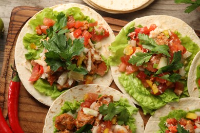 Delicious tacos with vegetables and meat on wooden table, flat lay